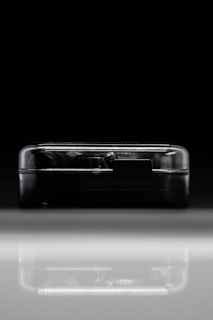A compact, semi-transparent black rectangular device is placed against a dark background and reflects on a shiny surface. The sleek lines and minimalist design suggest modern technology.
