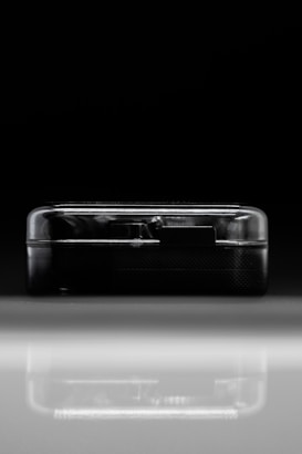 A compact, semi-transparent black rectangular device is placed against a dark background and reflects on a shiny surface. The sleek lines and minimalist design suggest modern technology.
