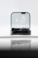 A sleek black gadget is partially enclosed in a clear rectangular case, reflecting on a glossy surface. The backdrop is soft and out-of-focus, creating a minimalist and modern aesthetic.