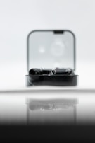 A sleek black gadget is partially enclosed in a clear rectangular case, reflecting on a glossy surface. The backdrop is soft and out-of-focus, creating a minimalist and modern aesthetic.
