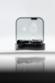 A sleek black gadget is partially enclosed in a clear rectangular case, reflecting on a glossy surface. The backdrop is soft and out-of-focus, creating a minimalist and modern aesthetic.