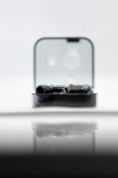 A sleek black gadget is partially enclosed in a clear rectangular case, reflecting on a glossy surface. The backdrop is soft and out-of-focus, creating a minimalist and modern aesthetic.