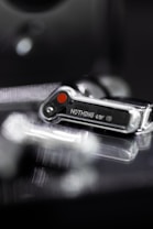 A close-up image of a metallic, high-tech object with a digital display showing the word 'NOTHING'. The object has a sleek, modern design with reflective surfaces and a noticeable red dot.