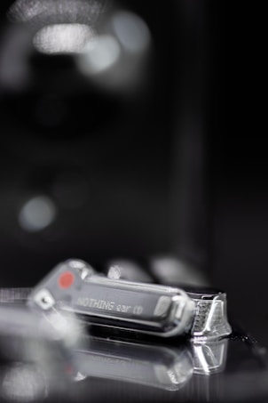 A close-up of a digital device with the word 'Nothing' inscribed on it, featuring a metallic and sleek design with a reflective surface. There are soft blurred lights in the background, adding a hint of mystery.