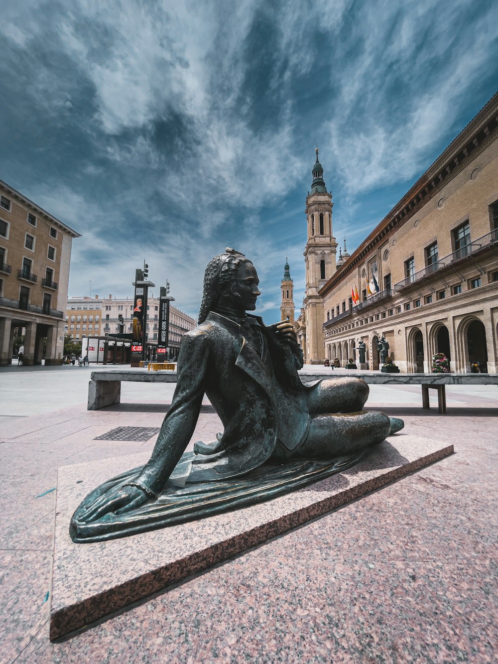 a statue of a person sitting on a stone bench in a city