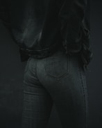 A person is wearing dark denim jeans and a matching denim jacket. The focus is on the lower back and hip area, showcasing the texture and fit of the clothing. The lighting is low, emphasizing shadows and details in the fabric.