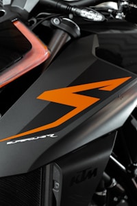 A close-up view of a motorcycle part featuring sleek black and orange design elements. The bodywork showcases the word 'SUPERDUKE' in stylized white text. The logo 'KTM' is also visible, indicating the motorcycle's brand. The image focuses on the angular lines and the modern, aggressive styling of the vehicle.