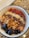 A bowl filled with a blend of ingredients including fresh blueberries, crunchy granola, cacao nibs, hemp seeds, and goji berries, all arranged on a layer of purple acai or smoothie blend. The mixture is presented in a white bowl with a black rim, set on a marbled surface.
