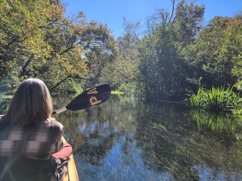 A kayaker paddling through crystal-clear water surrounded by lush greenery.