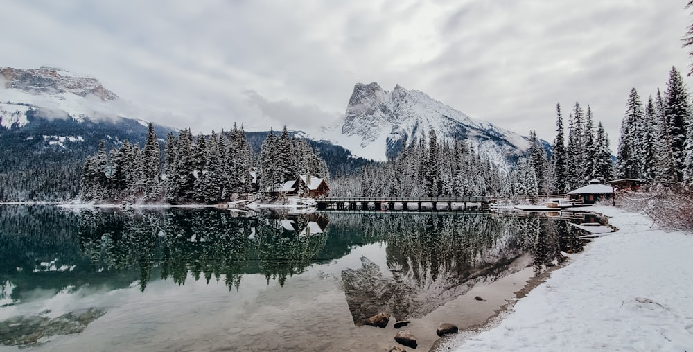 a lake with a house and snowy mountains in the background