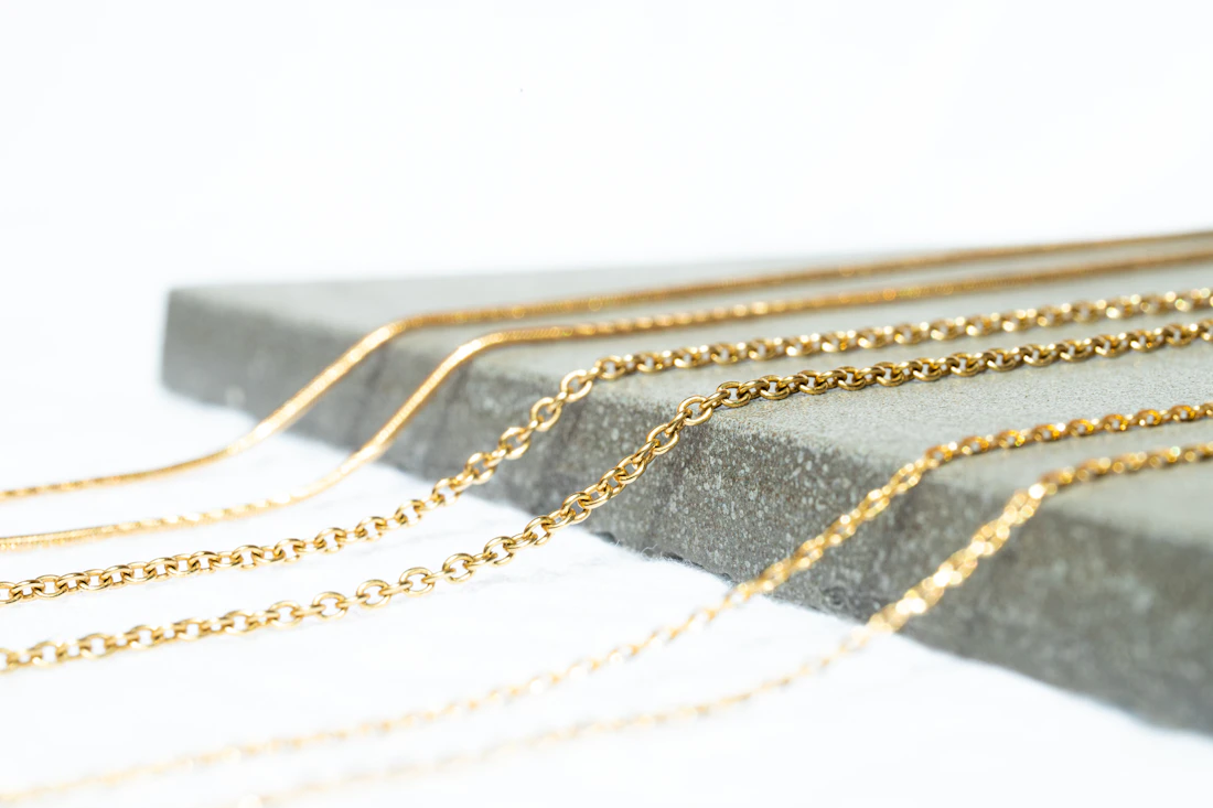 Layered fine gold chains on a pale concrete surface