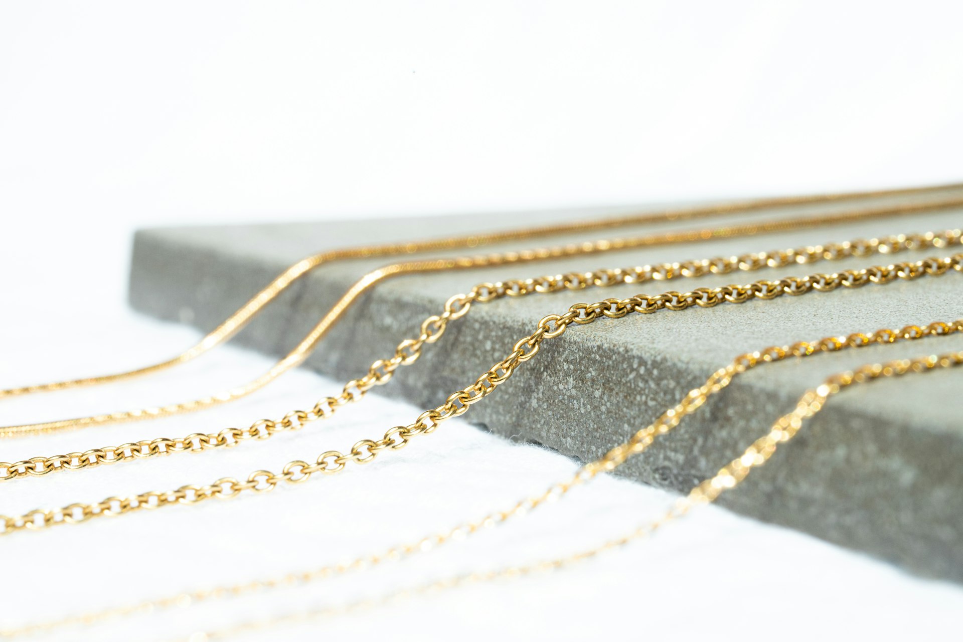 Layered fine gold chains on a pale concrete surface