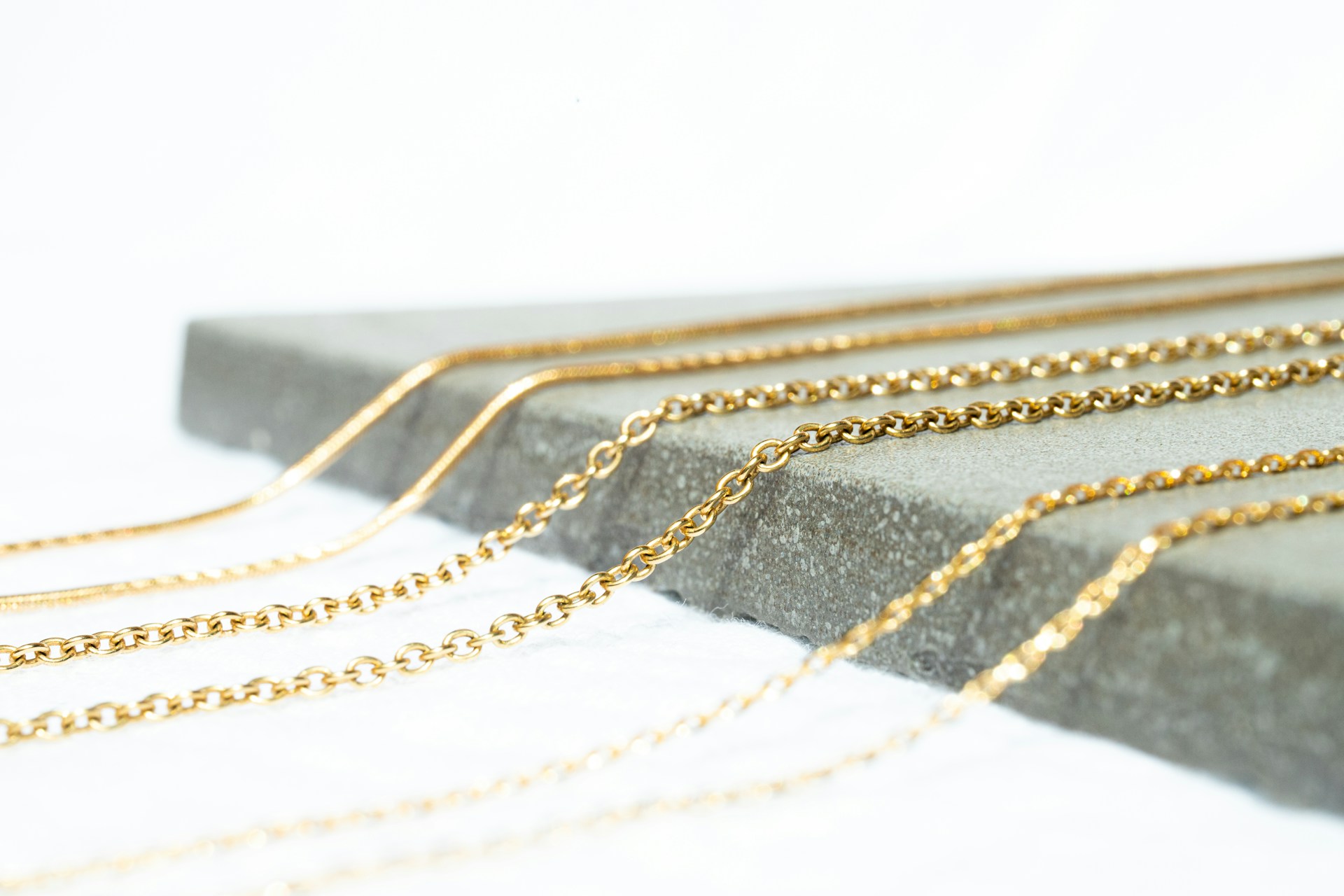 Layered fine gold chains draped over a pale stone slab