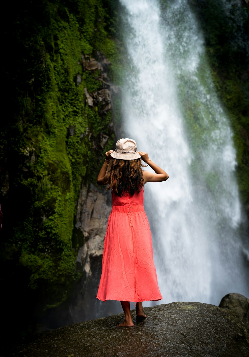 a girl in a red dress standing in front of a waterfall