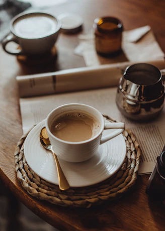 A cozy coffee-themed accessory setup with mugs, coasters, and bags arranged on a wooden table.