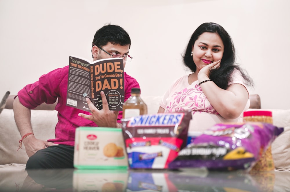 a man and woman sitting at a table with boxes and a bottle of liquor