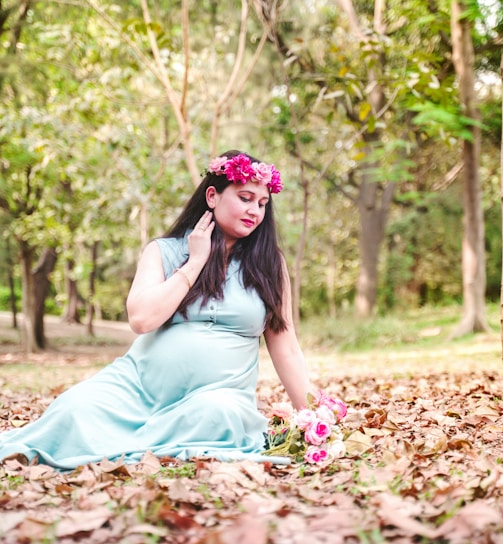 a person in a blue dress sitting on leaves with a flower in the hair