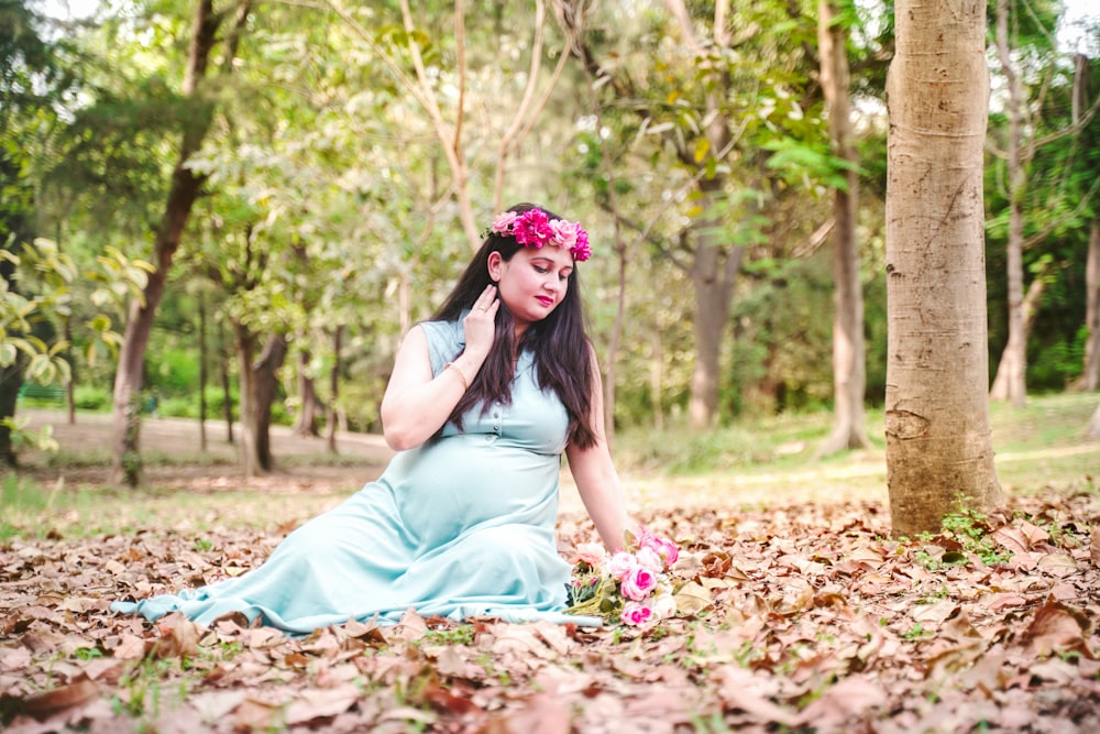 a person in a blue dress sitting on leaves with a flower in the hair