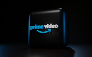 A dark background contrasts with a three-dimensional, illuminated logo in the center. The logo is composed of the words 'prime video' in bold, blue lettering with a distinctive smile-shaped arrow underneath, casting subtle shadows.
