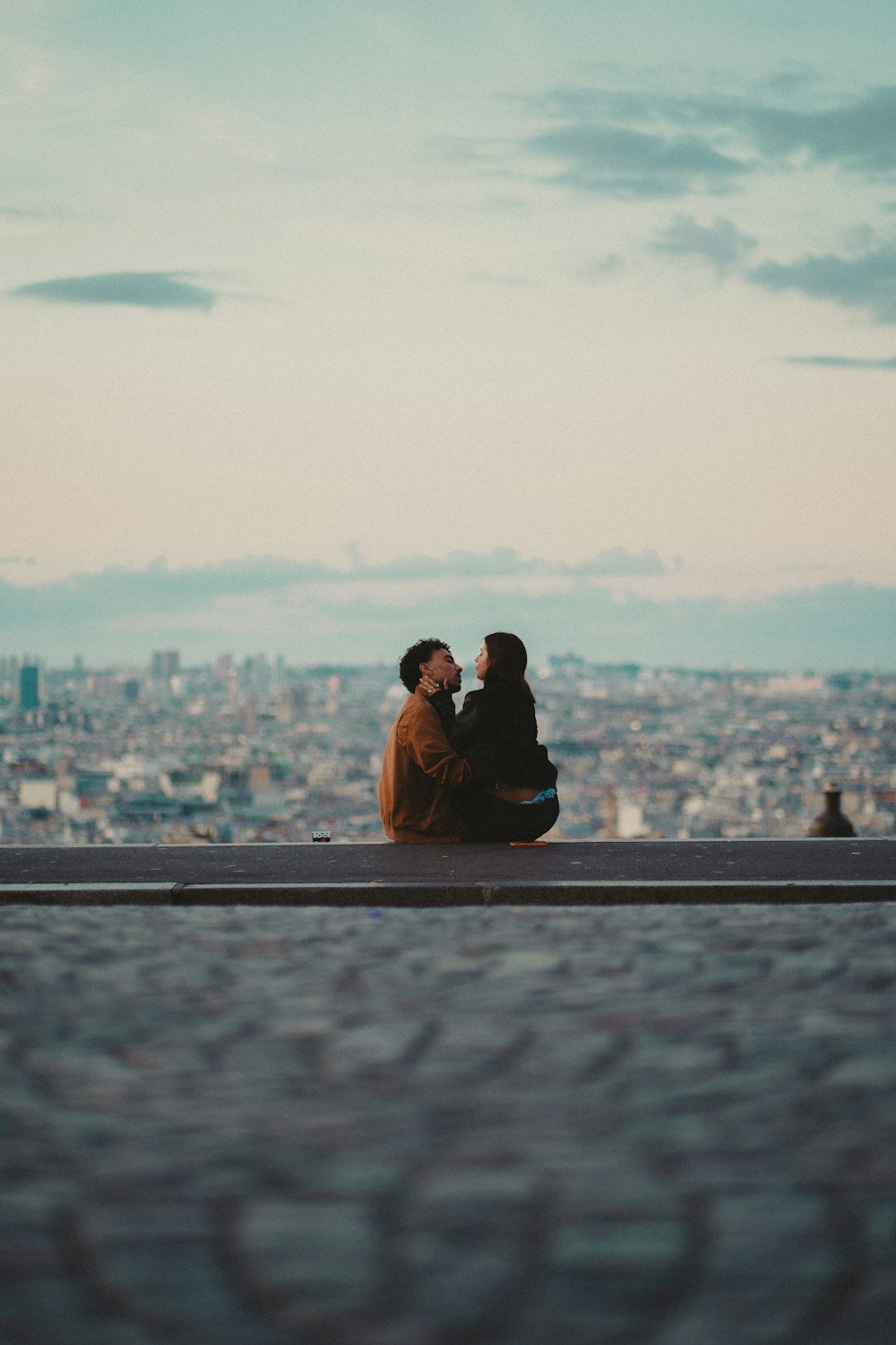 a man and woman sitting on a ledge overlooking a city