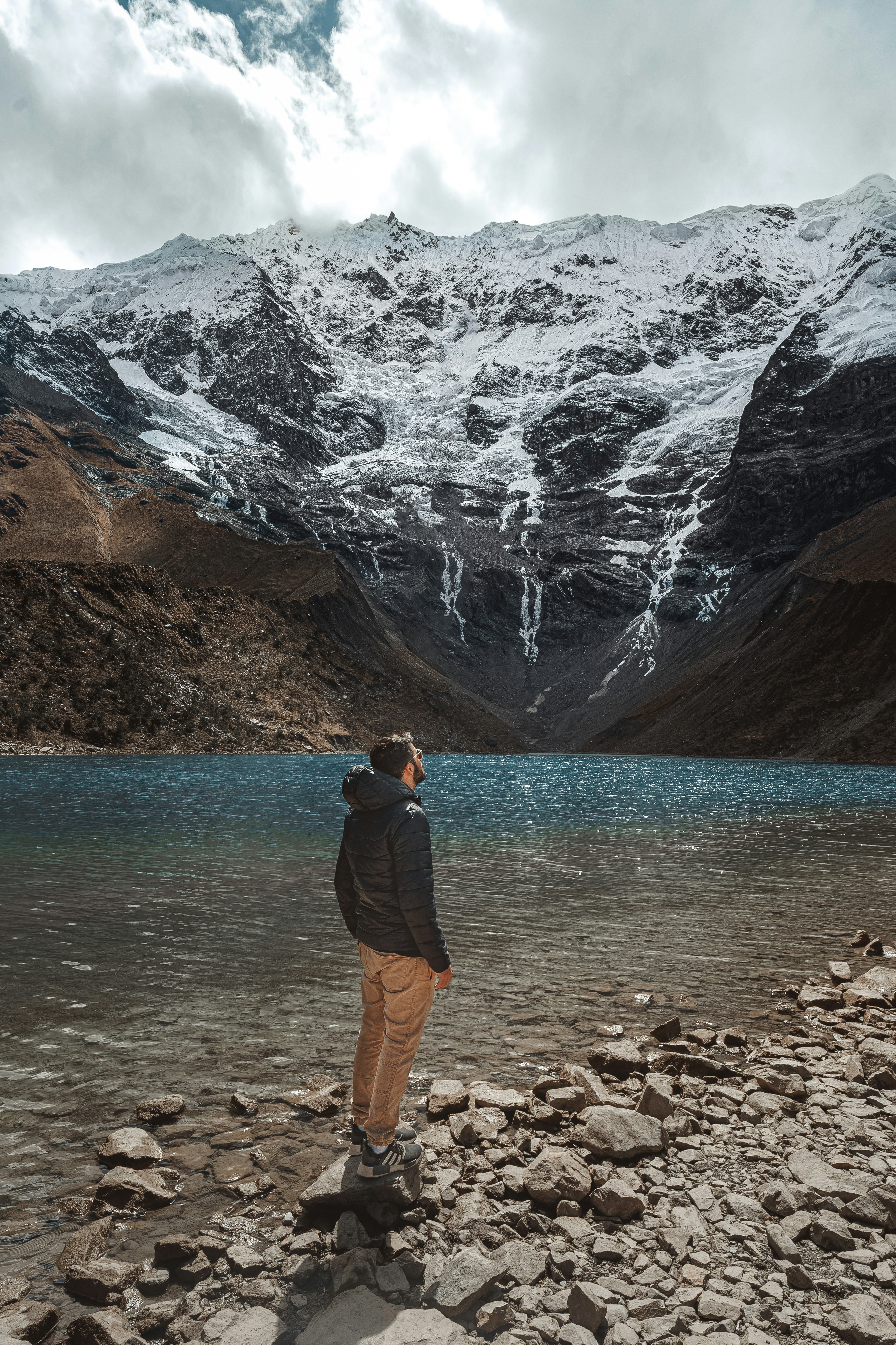 a man standing on a rocky shore with a mountain in the background