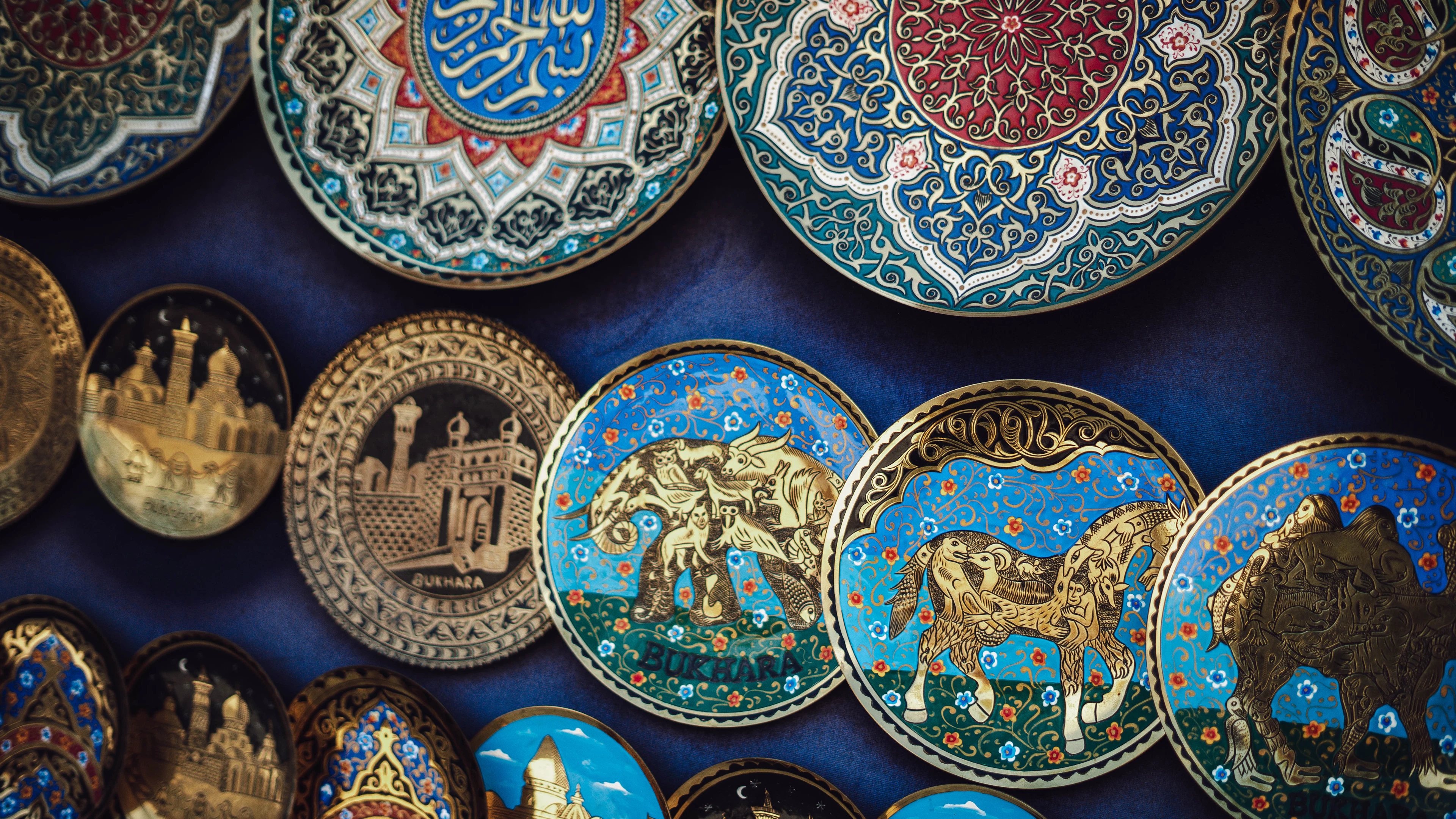 Hand-painted Uzbek ceramics hung on a wall in Bukhara, glazed in deep blue and gold and decorated with elephants, horses and looping calligraphy.