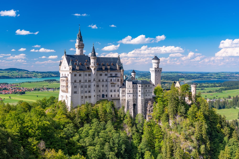 a castle with a clock on the tower of the city with Neuschwanstein Castle in the background