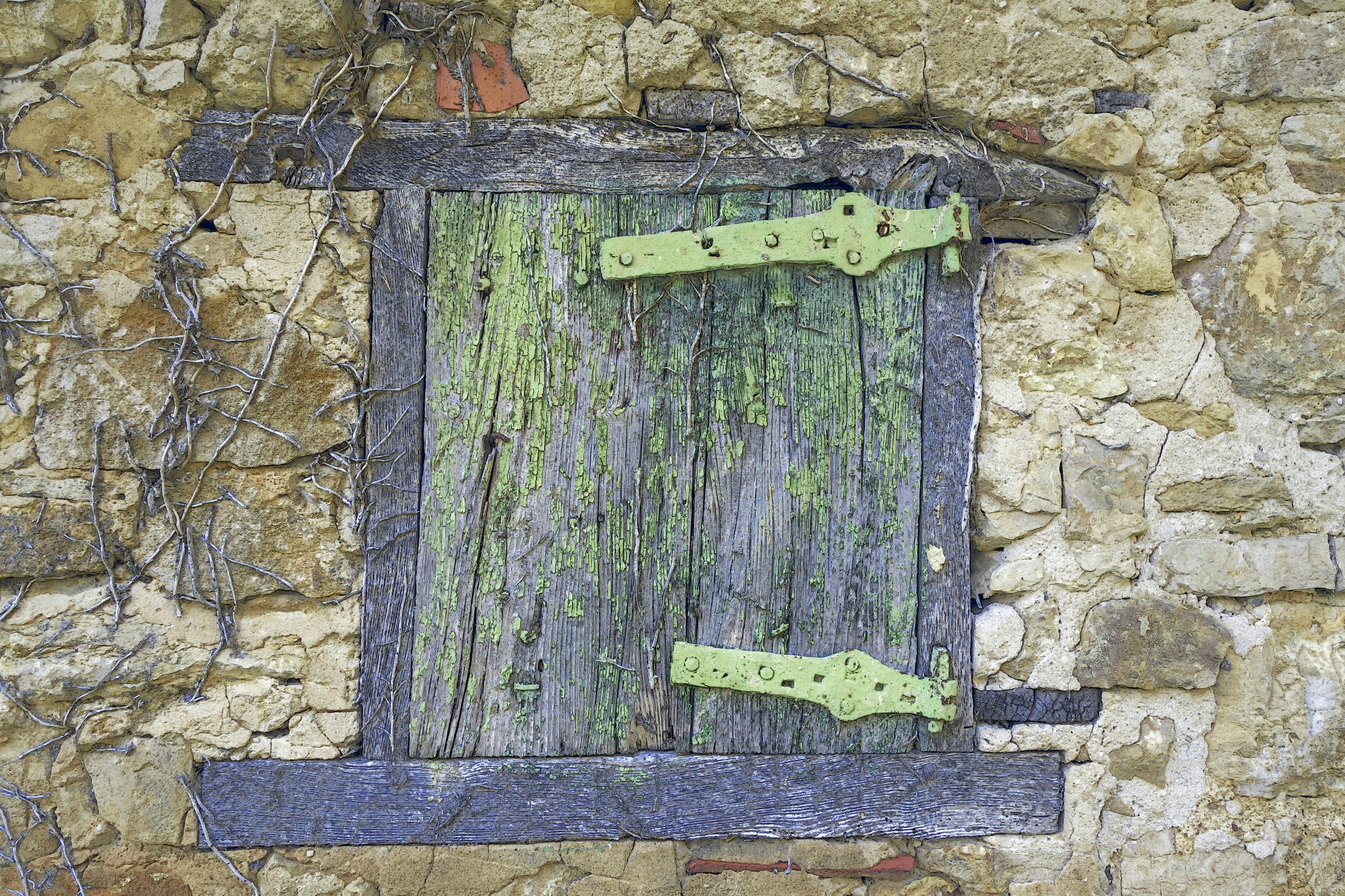Volet de bois vert écaillé dans un mur de pierre