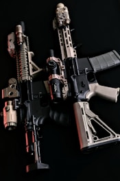 Two tactical rifles are displayed side by side against a dark background. They are equipped with various attachments including scopes and flashlights, featuring a combination of black and tan colors.