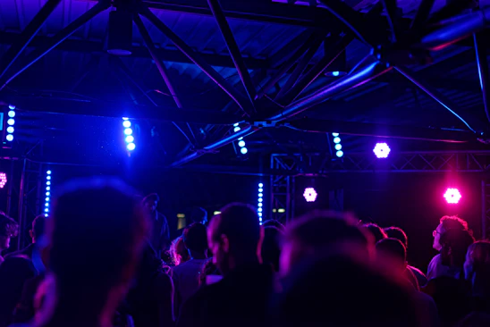 Dark industrial rave scene with intense lighting and crowd immersed in music.