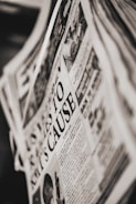 A close-up of a newspaper page with a prominent headline. The text is printed in black and white, and the layout includes columns of articles and an image depicting a person and a public scene. The newspaper appears slightly tilted.