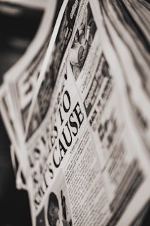 A close-up of a newspaper page with a prominent headline. The text is printed in black and white, and the layout includes columns of articles and an image depicting a person and a public scene. The newspaper appears slightly tilted.