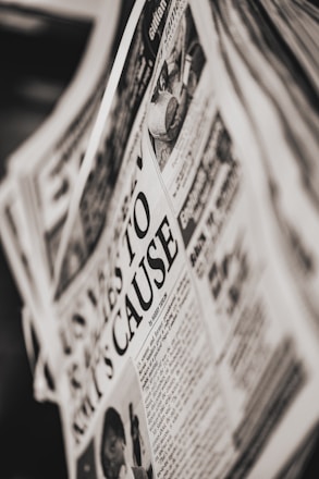 A close-up of a newspaper page with a prominent headline. The text is printed in black and white, and the layout includes columns of articles and an image depicting a person and a public scene. The newspaper appears slightly tilted.