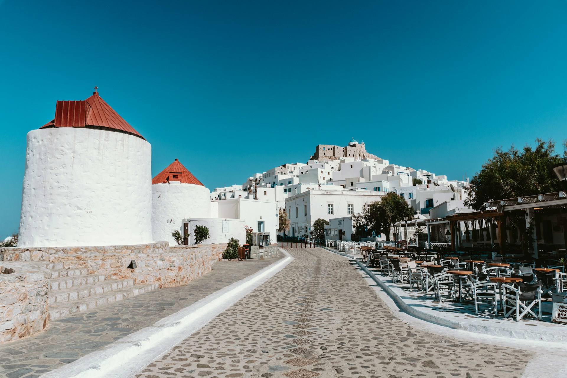 a stone walkway with tables and chairs on it and buildings in the background
