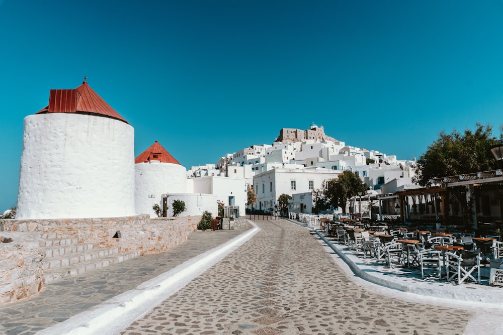 a stone walkway with tables and chairs on it and buildings in the background