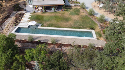 An aerial view of a backyard featuring a custom-shaped pool and a fire pit area.