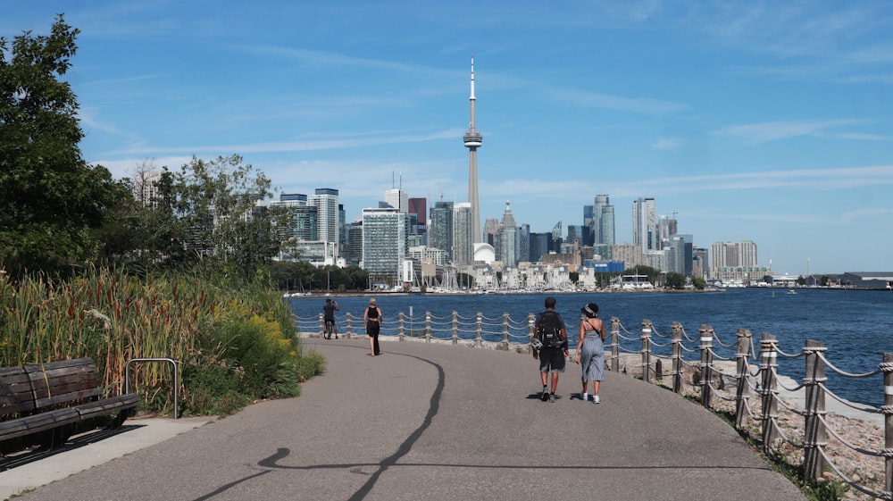 people walking on a path by a body of water with a city in the background