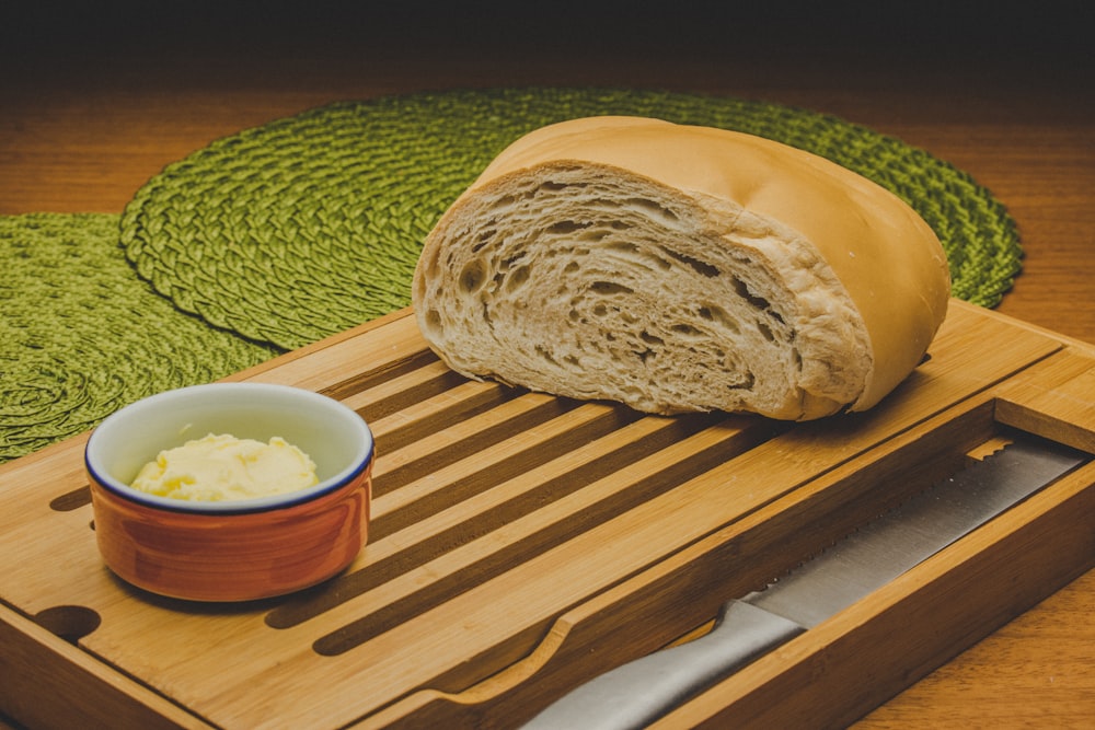 a loaf of bread on a cutting board next to a bowl of butter