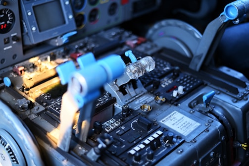 A detailed view of an aircraft cockpit with a focus on the central control panel and throttle levers. Various buttons, switches, and labels are visible with a digital display and indicators. The blue and metallic tones dominate the color scheme, reflecting a technical and industrial design.