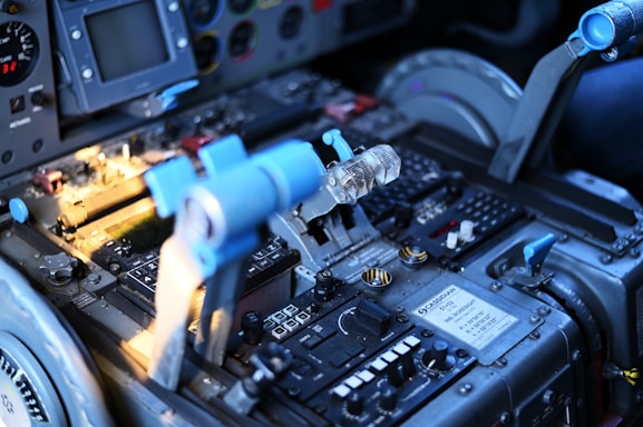 A detailed view of an aircraft cockpit with a focus on the central control panel and throttle levers. Various buttons, switches, and labels are visible with a digital display and indicators. The blue and metallic tones dominate the color scheme, reflecting a technical and industrial design.