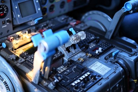 A detailed view of an aircraft cockpit with a focus on the central control panel and throttle levers. Various buttons, switches, and labels are visible with a digital display and indicators. The blue and metallic tones dominate the color scheme, reflecting a technical and industrial design.