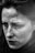 A close-up black and white portrait of a person with freckles, expressing a contemplative or pensive mood. The image highlights texture and emotion through the use of shadows and light.