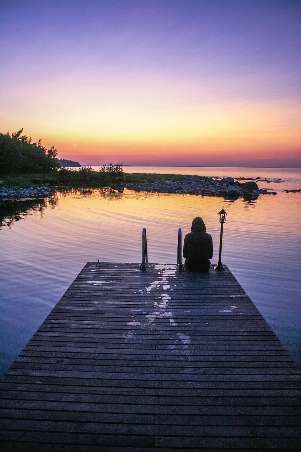 a person sitting on a dock looking at the sunset