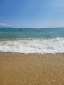 A wide shot of a sandy beach with gentle waves under a clear blue sky.