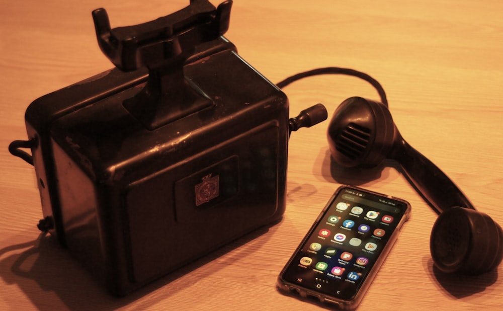 a black phone next to a black box with a cord