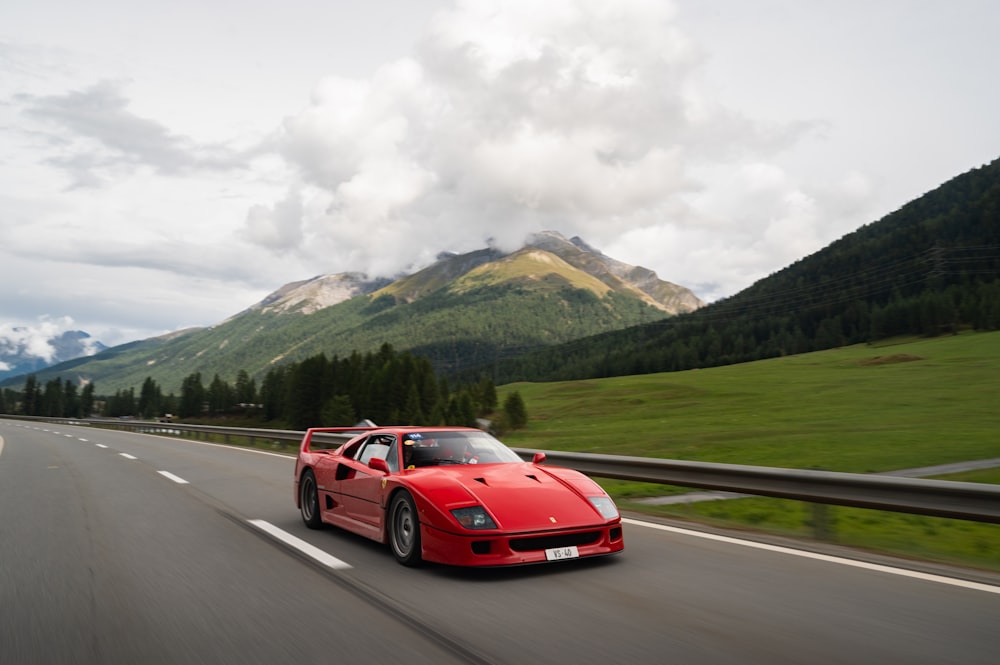 a red sports car driving on a road with mountains in the background