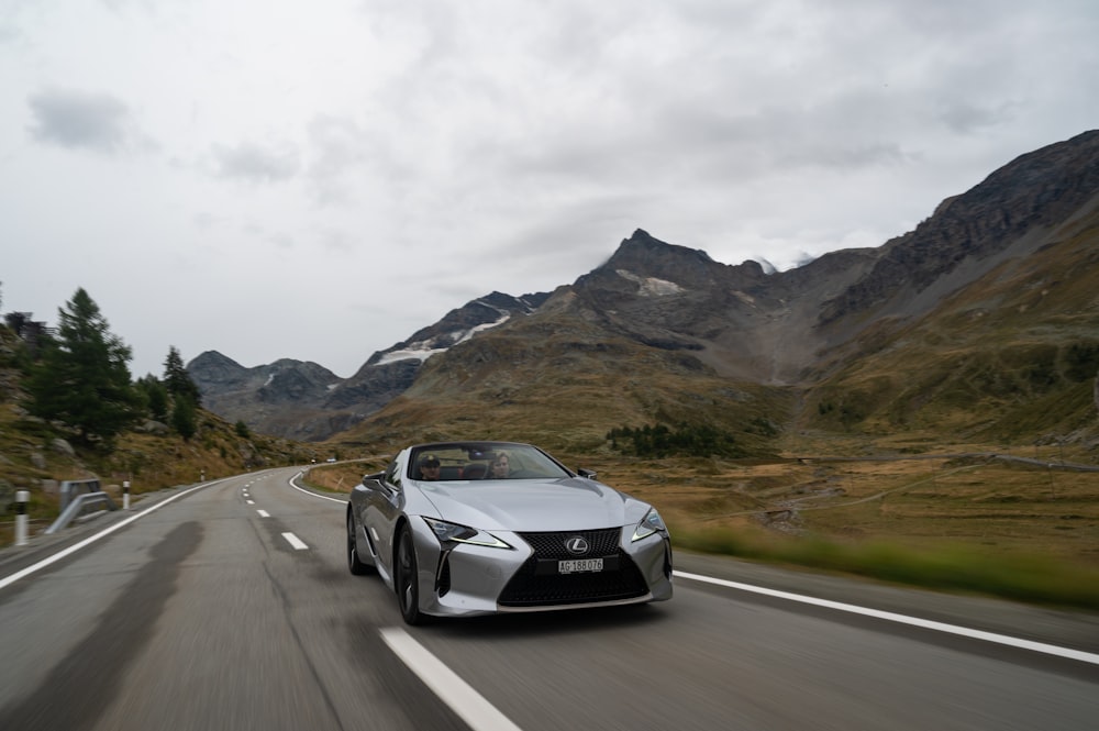 a black sports car driving on a road with mountains in the background