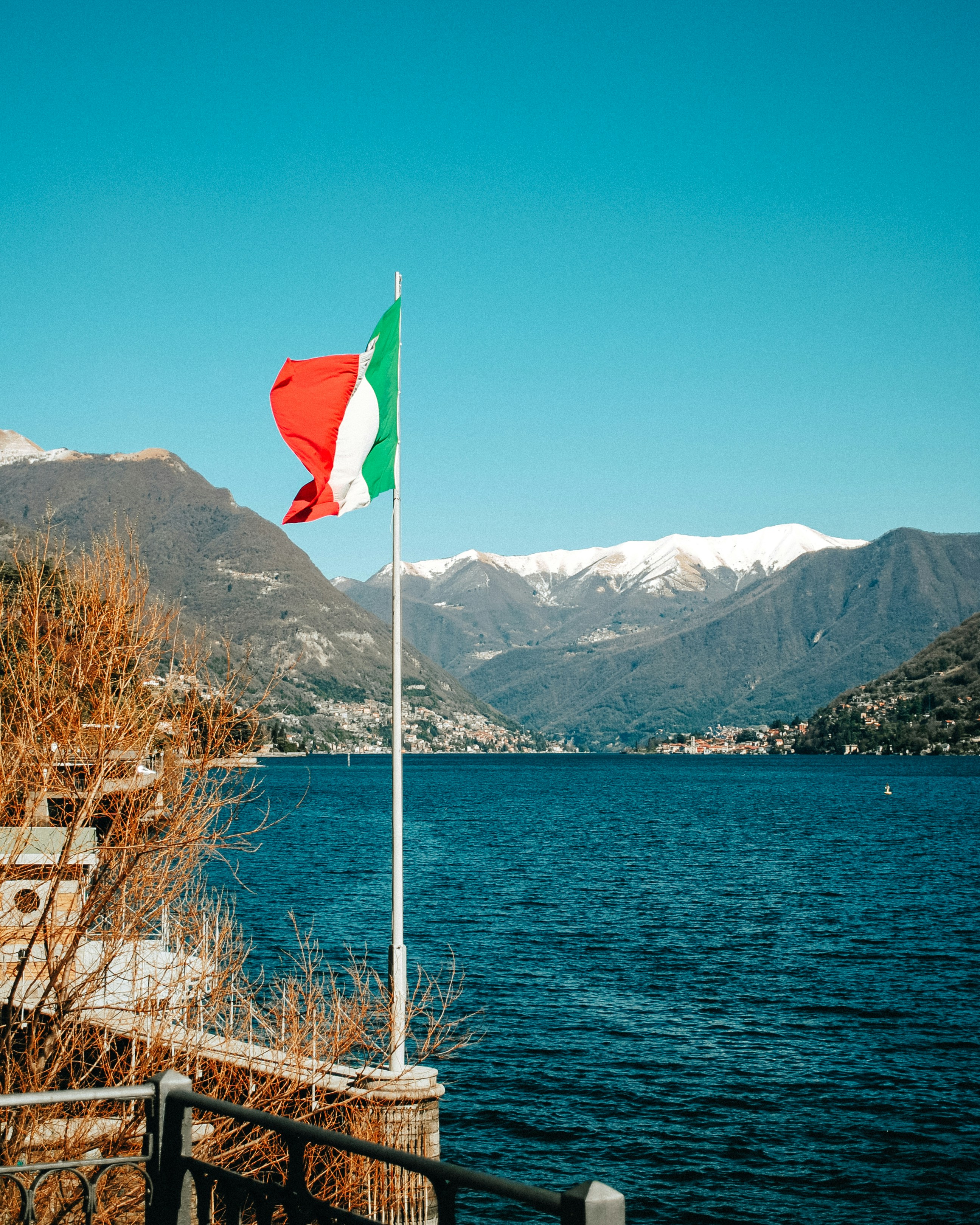 a flag on a pole by a body of water with mountains in the background