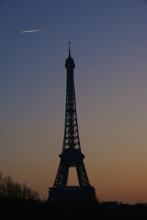 Airplane flying over the Eiffel Tower at sunset.