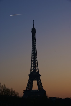Airplane flying over the Eiffel Tower at sunset.